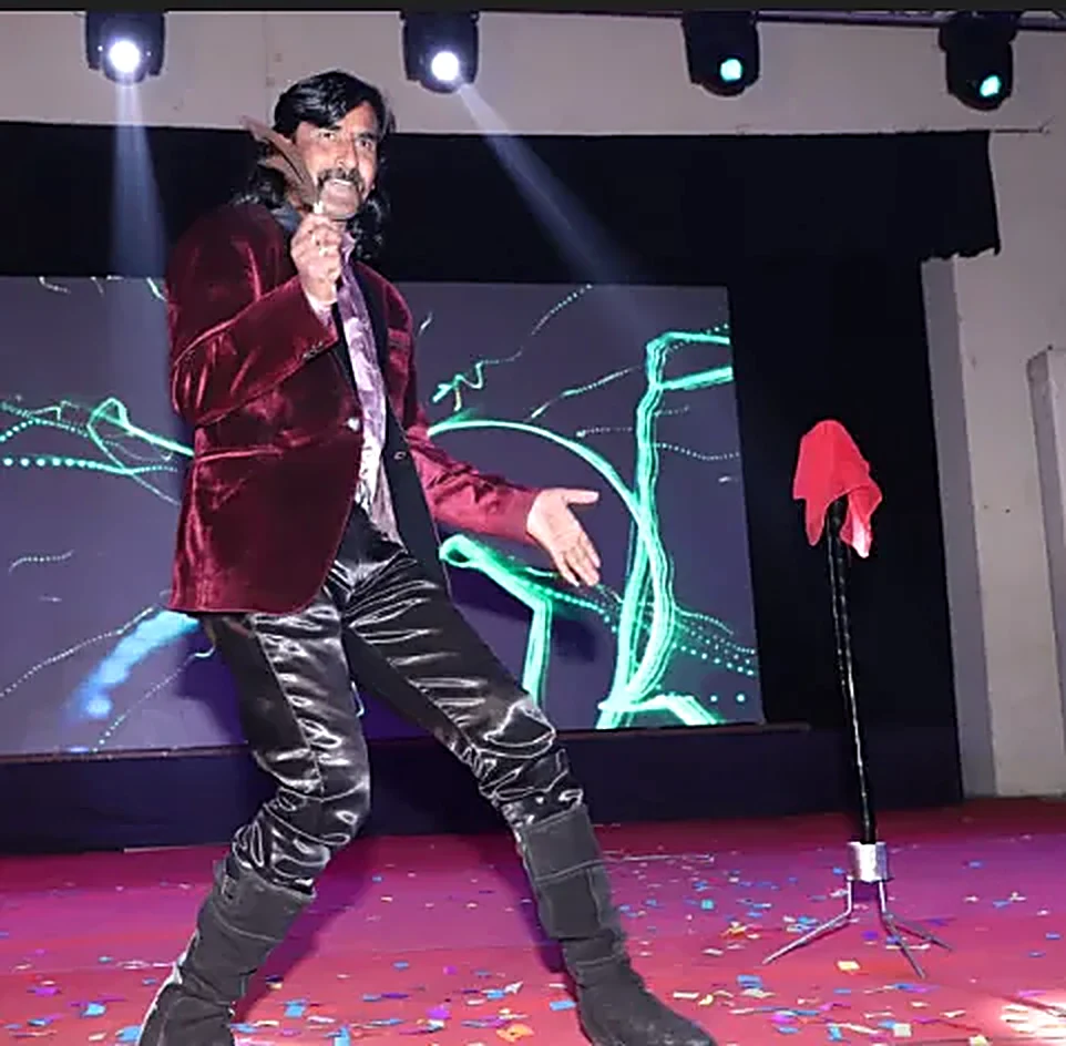 Jadugar Rajtilak performing live on stage in his maroon velvet blazer as gold confetti rains down around him